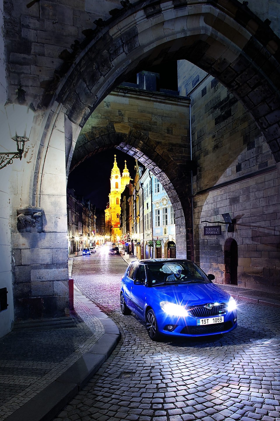 Blå bil parkerad under ett valv på en kullerstensgata i Prag på natten