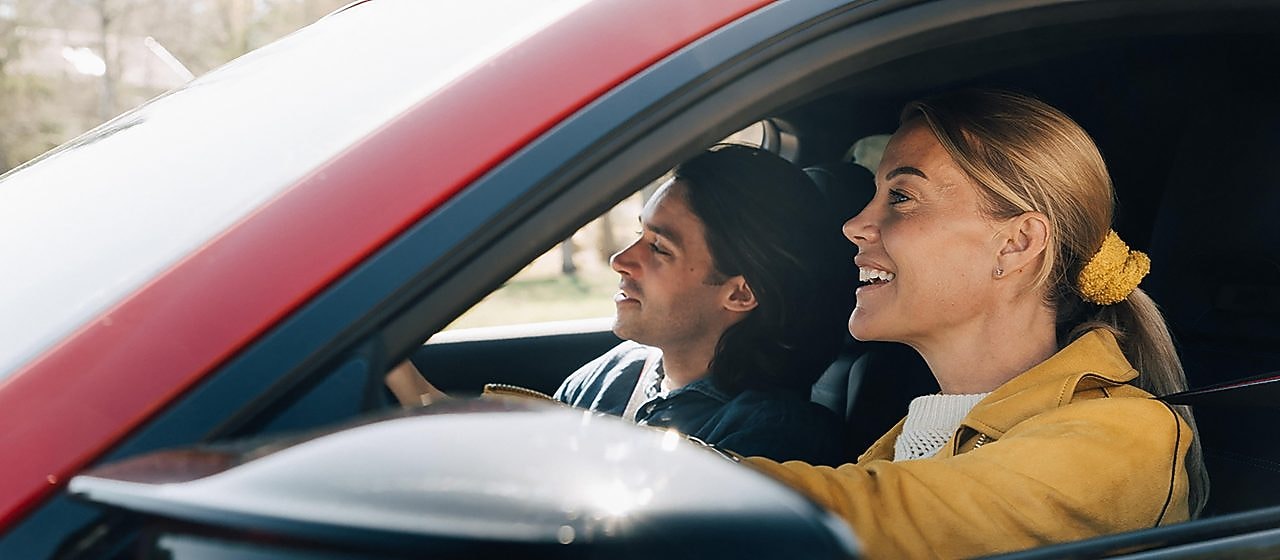 En kvinna och en man åker i en röd bil
