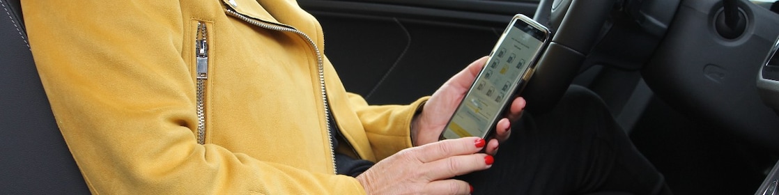En kvinna sitter i bilen håller en mobiltelefon med St1 Mobility appen.