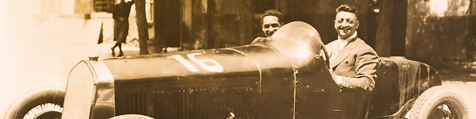 Svartvit bild på Enzo Ferrari som sitter i en av de första Ferrari-bilarna