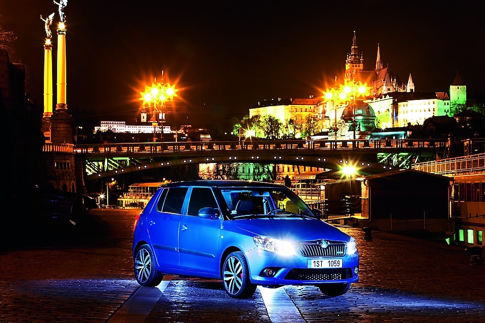 Blå bil parkerad på en gata i Prag nattetid med en bro och ett slott i bakgrunden