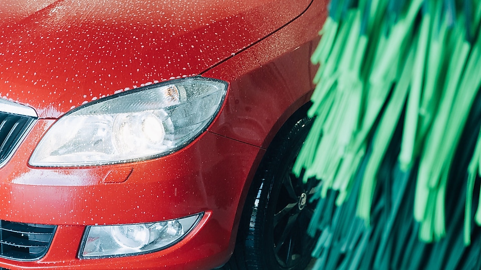 En röd bil tvättas i en Shell biltvätt