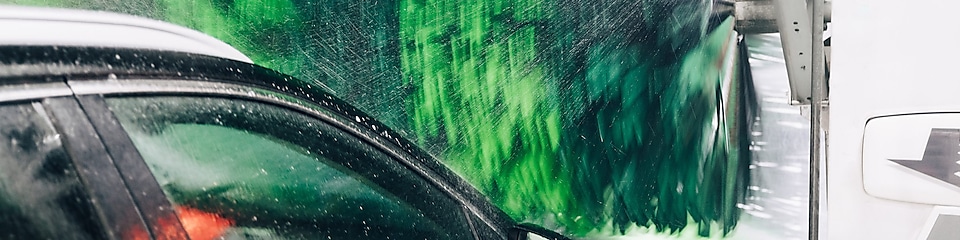 En svart bil tvättas in en biltvätt vid Shell. Vatten stänker från en grön biltvättsborste.